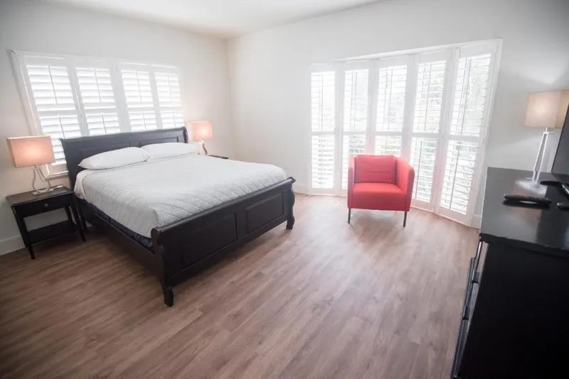 Suite King bed and red armchair by a bay window with white plantation shutters